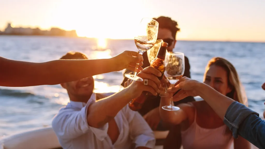 Group of people toasting with drinks on a boat at sunset.
